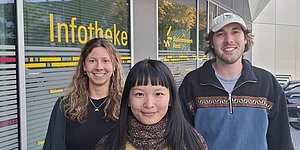 Foto: Drei Personen vor einer Glasscheibe mit Aufdruck Infotheke