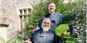 Foto: Zwei Koeche vom Team Mensa Witzenhausen vor Mensa-Gebaeude