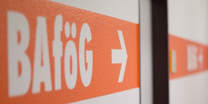 Symbolgrafik: weisse Schrift BAföG mit Pfeil auf orangefarbenem Untergrund