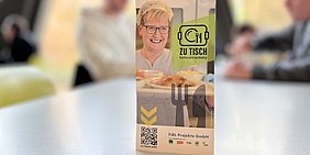 Foto: Tischaufsteller mit Aufdruck ZU TISCH vor Mensa-Hintergrund