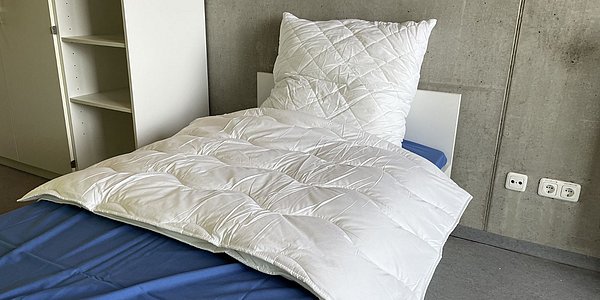 Ein Foto von den Inhalten des Starterpakets Nr. 4. Zu sehen sind eine Bettdecke und ein Kissen, die auf einem Bett liegen.