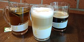 Foto: Drei Glastassen mit Aufdruck, gefuellt mit (von links) Tee, Latte Macchiato, Kaffee