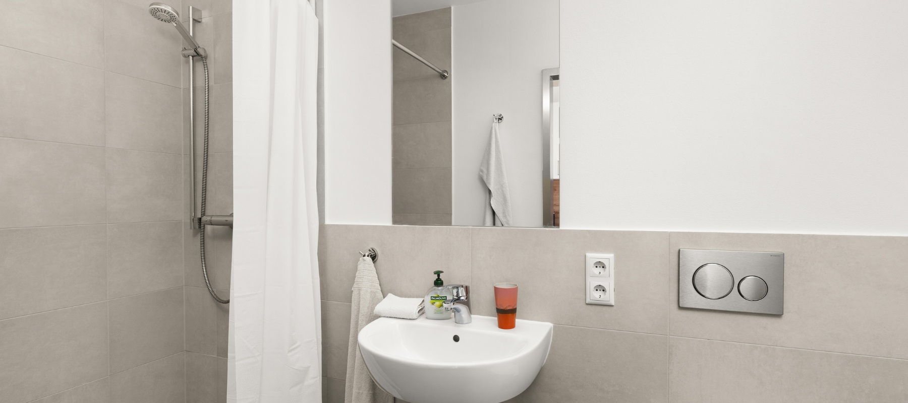 Bad eines Einzelapartments. Zu sehen ist eine moderne Dusche sowie ein Waschbecken.