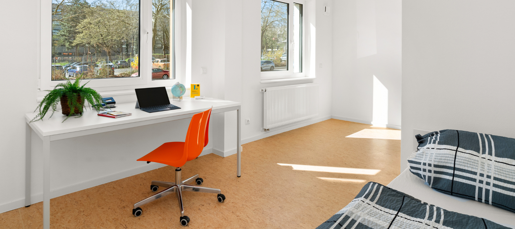 Blick in ein Einzelapartment. Zu sehen ist ein Schreibtisch mit einem Bürostuhl und ein Bett.