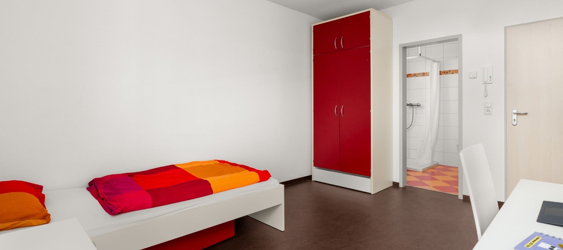 Foto aus dem Zimmer eines Doppelapartments. Zu sehen sind ein Bett und ein Kleiderschrank.
