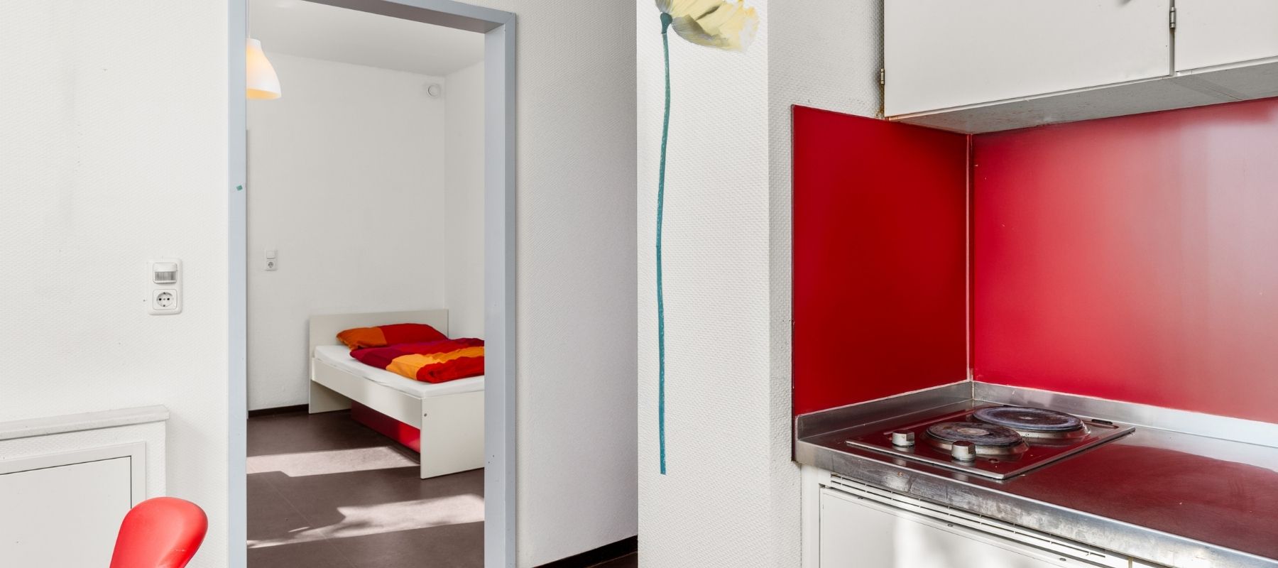 Foto von der Küchenzeile einer WG. Neben der Küchenzeile ist eine offene Türe, die zu einem Einzelapartment führt.