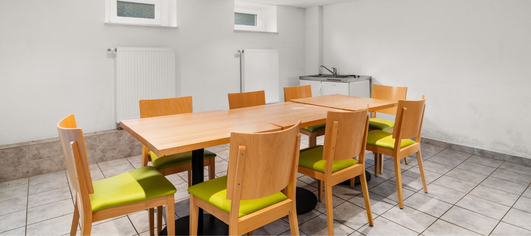 Foto vom Gemeinschaftsraum im Keller des Wohnheims. Zu sehen sind Stühle, die um einen Tisch angeordnet sind.