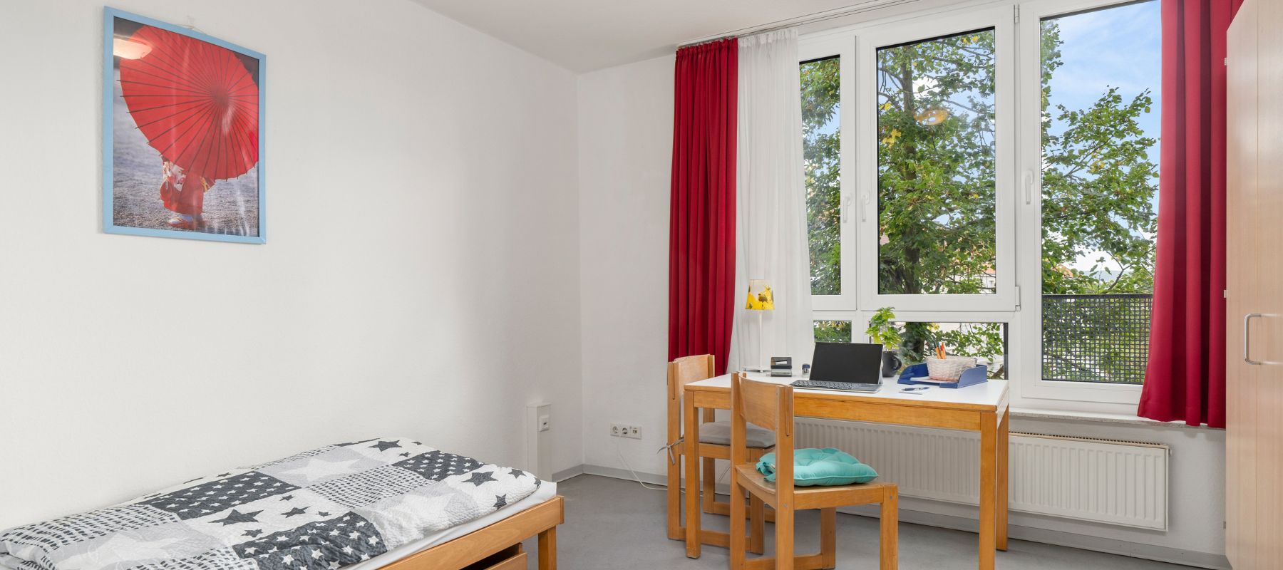 Foto eines Einzelapartments mit einem Schreibtisch am Fenster und einem Bett.