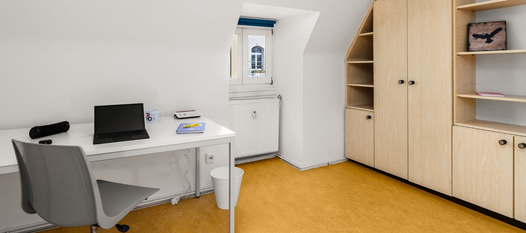 WG-Zimmer in der Hegelsbergstraße 22. Zu sehen sind ein Schreibtisch mit Stuhl sowie eine Schrankwand.