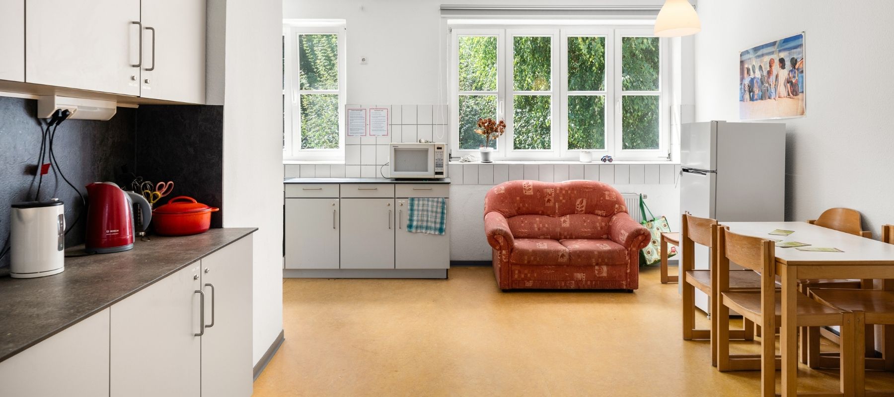 Große, helle WG-Küche der Hegelsbergstraße 22a. Zu sehen sind eine Küchenzeile, eine Spüle im Hintergrund, ein Sofa, ein Kühlschrank sowie ein Esstisch mit mehreren Stühlen.