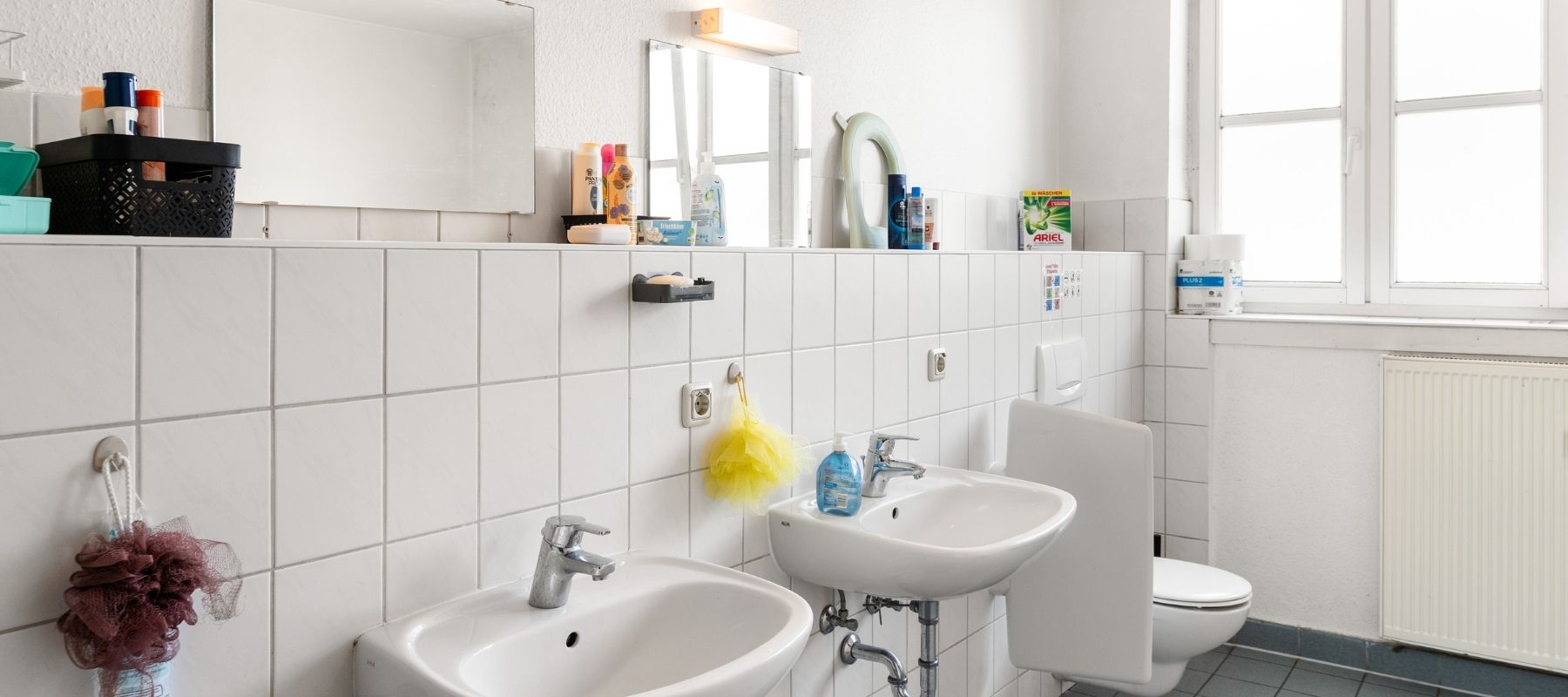 WG-Bad in der Hegelsbergstraße 22a. Zu sehen sind zwei Waschbecken, zwei Spiegel, eine Toilette und ein großes Fenster.