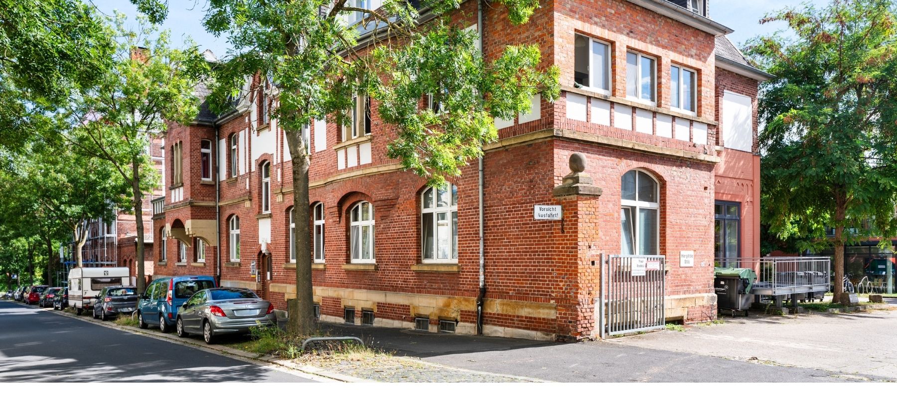 Die Straße vor der Hegelsbergstraße 24. Zu sehen sind parkende Autos sowie hohe Bäume.