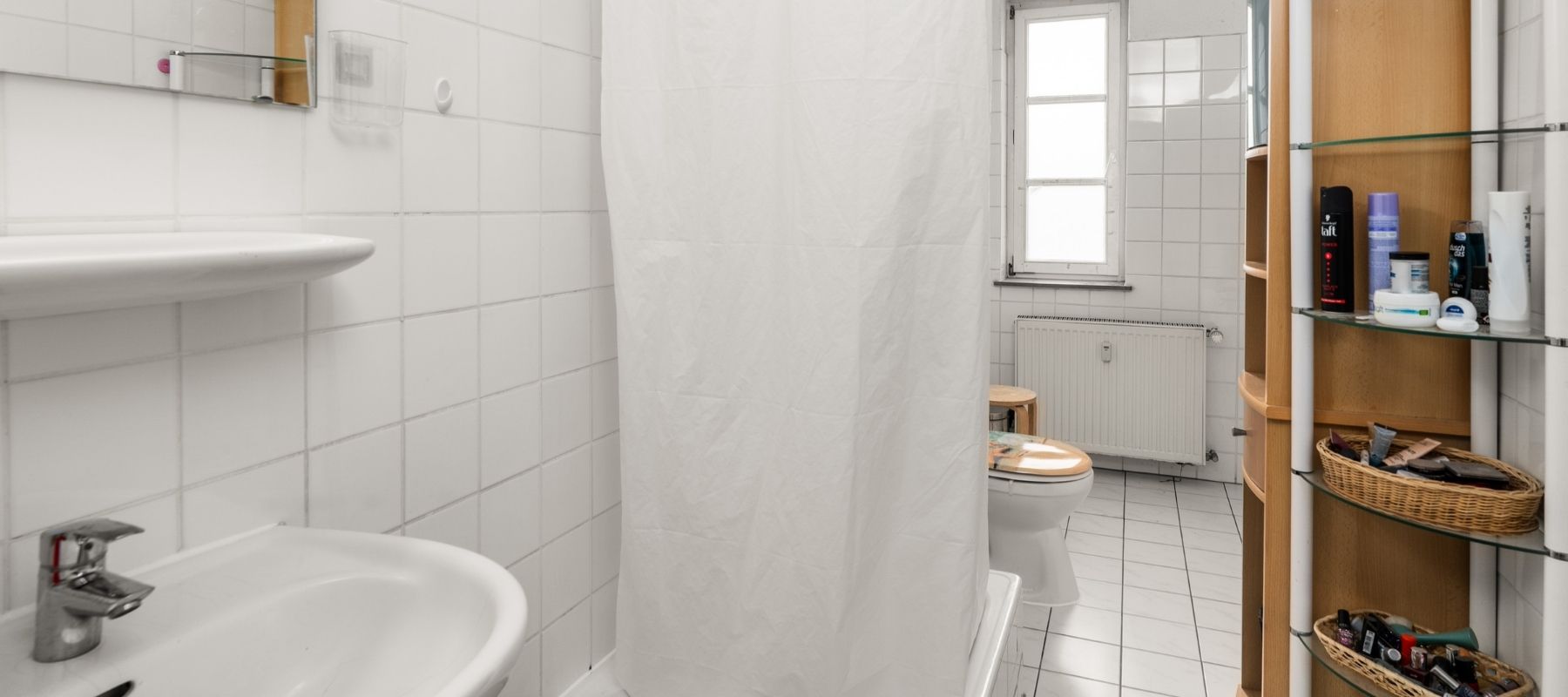 WG-Bad in der Hegelsbergstraße 24. Zu sehen sind ein Waschbecken, ein Regal, eine Dusche sowie eine Toilette. Im Hintergrund ist ein Fenster.