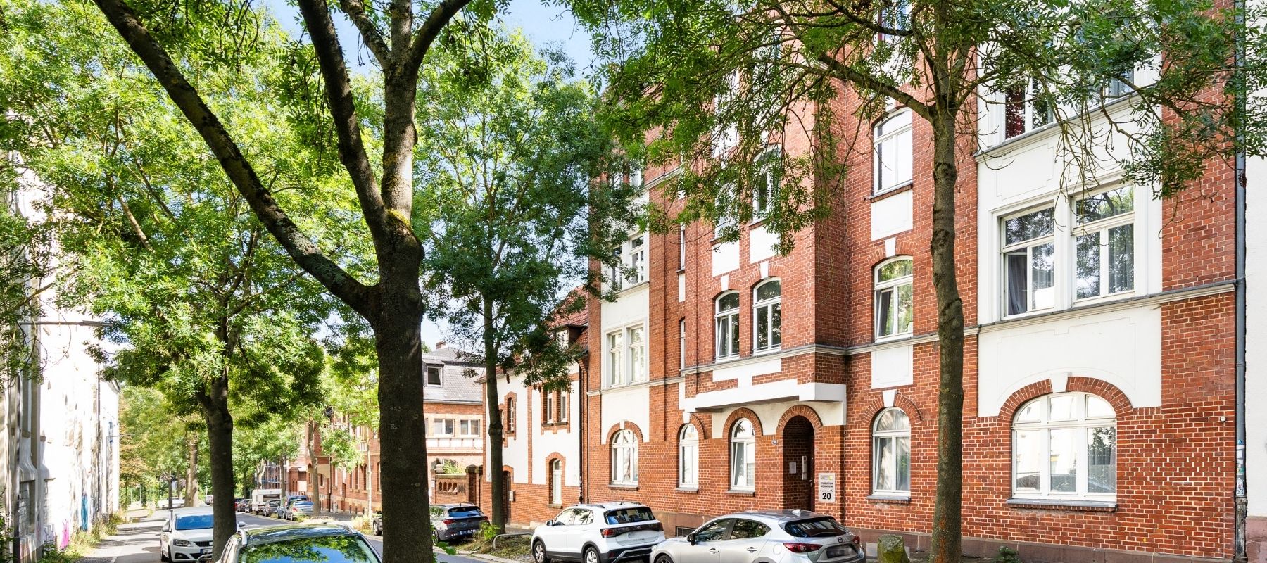 Die Straße vor der Hegelsbergstraße 20. Zu sehen sind große Bäume und parkende Autos.