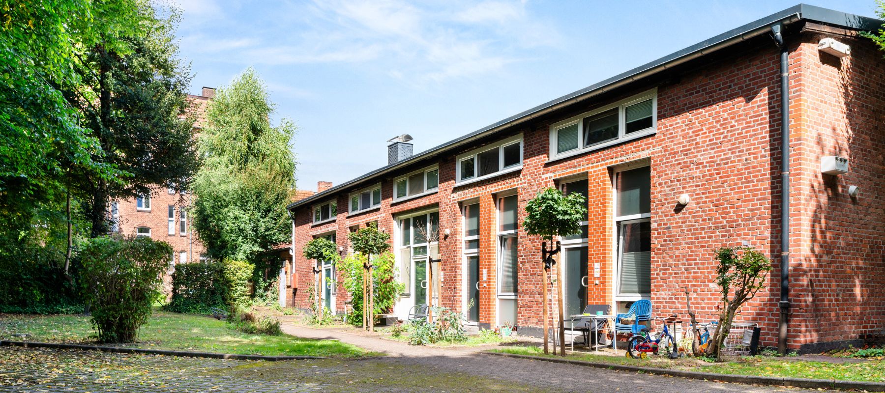 Foto von der Rückseite des Gebäudes. Zu sehen sind die Zugänge der Studiowohnungen zum Gartenbereich.