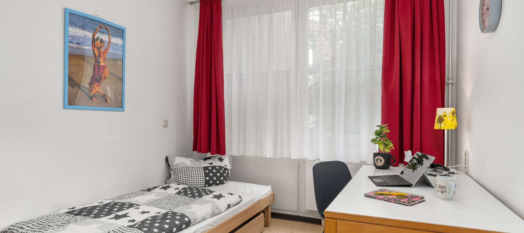 Einzelzimmer in WG mit Schreibtisch, Bett und einem Bild an der Wand.