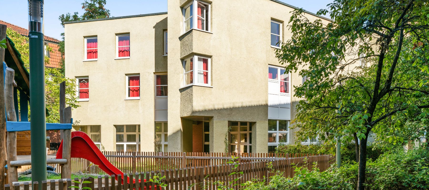 Rückseite des Wohnheims Arnold-Bode-Straße 4, davor ein Spielplatz, auf dem eine Rutsche zu sehen ist.