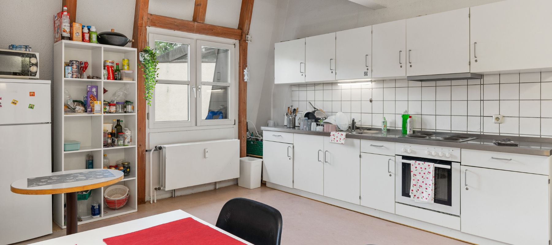 Gemeinschaftsküche einer WG: Blick vom Esstisch auf die große Küchenzeile mit Backofen und Herd.