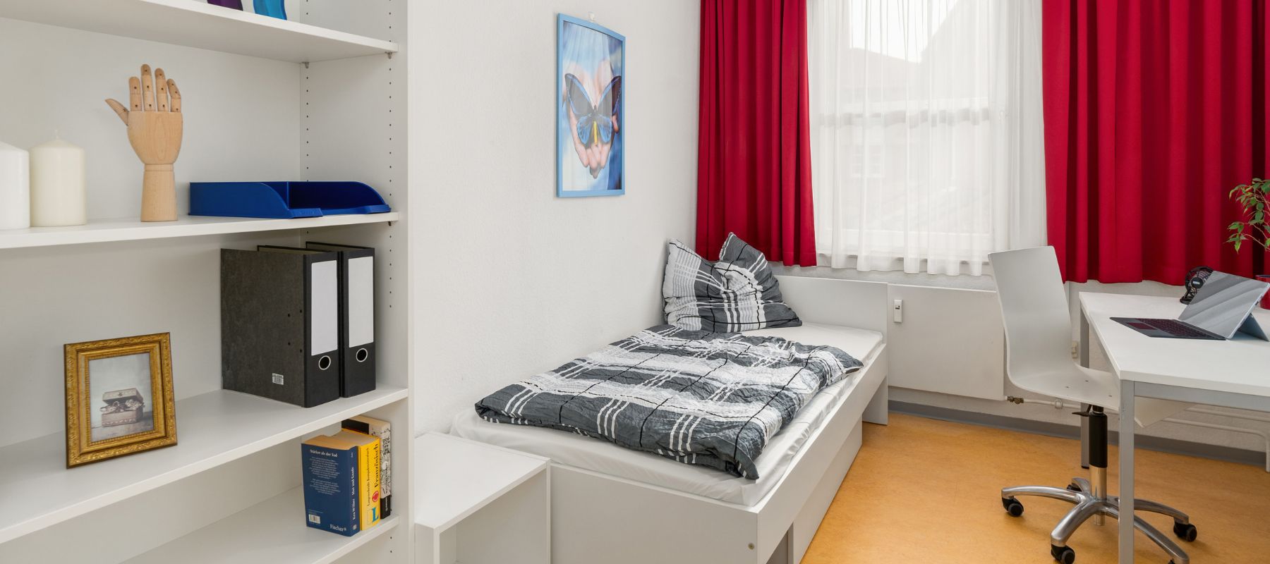 Einzelapartment mit Bücherregal, Bett und Schreibtisch.