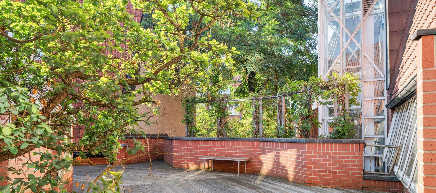 Dachterrasse des Wohnheims Arnold-Bode-Straße 4. Zu sehen sind ein Holzboden, ein gemauertes Geländer und eine Sitzbank.