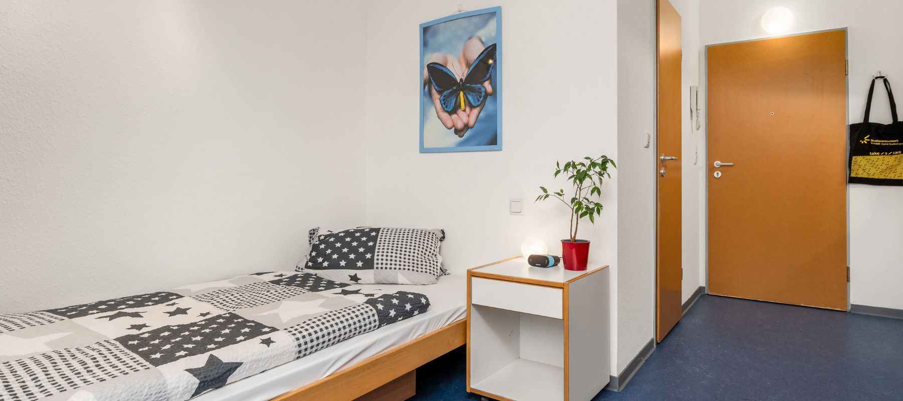 Einzelapartment im Wohnheim. Zu sehen ist der Blick in Richtung Wohnungstüre. Mit im Bild ist außerdem das Bett mit einem Beistelltisch daneben.