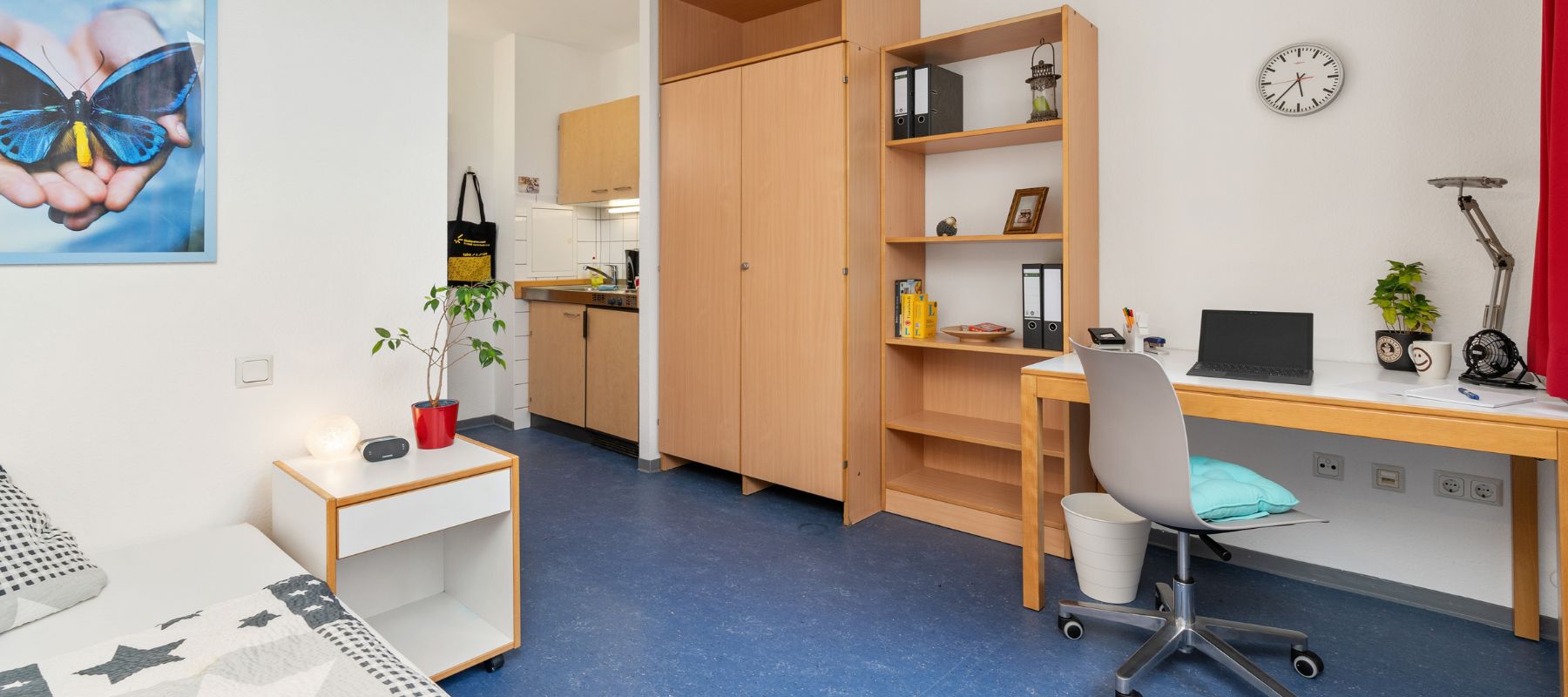 Einzelapartment im WOhnheim. Gezeigt wird der Blick vom Bett auf Schreibtisch, Bücherregal, Kleiderschrank und Küchenzeile. 