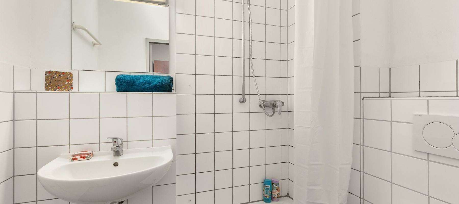 Badezimmer eines Einzelapartments. Zu sehen sind Waschbecken, Dusche und der Spülkasten einer Toilette.