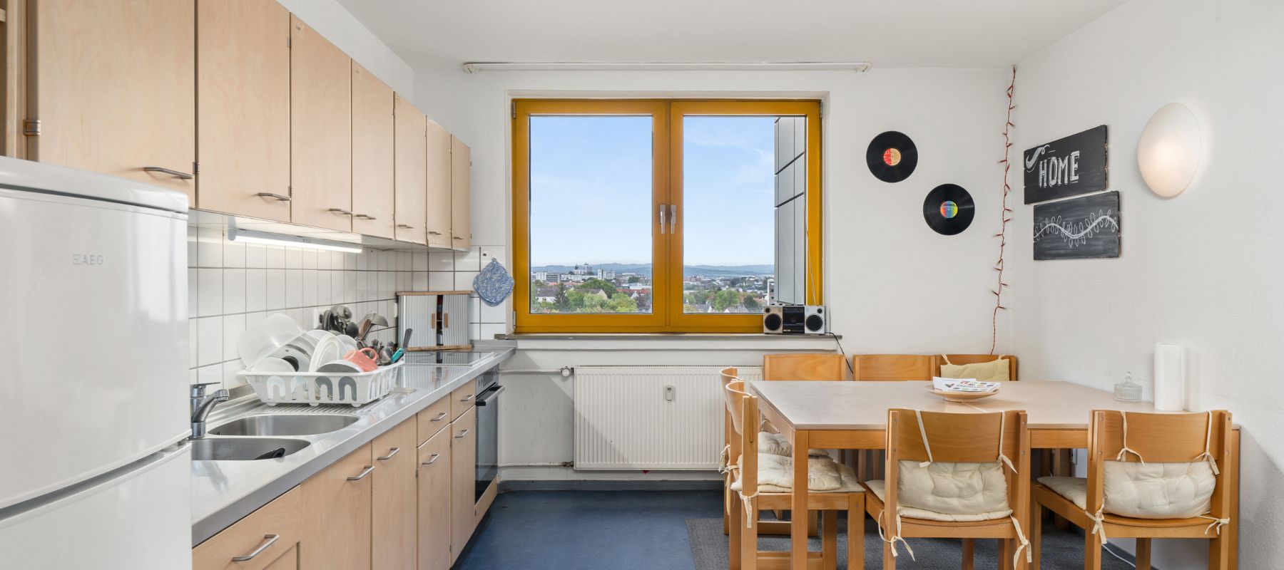 Gemeinschaftsküche einer WG mit großer Küchenzeile, einem großen Esstisch mit Stühlen. Am Ende der Küche ist ein Fenster, von dem aus man einen Weitblick über Kassel hat.