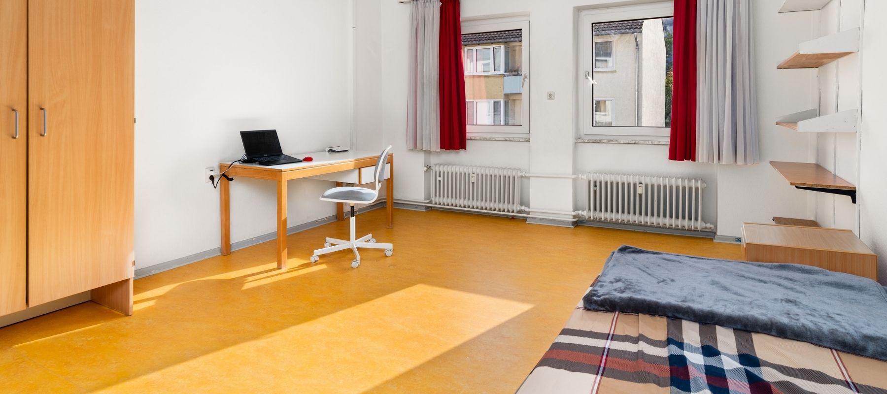 WG-Zimmer mit Bett, Kleiderschrank, Schreibtisch und Schreibtischstuhl.