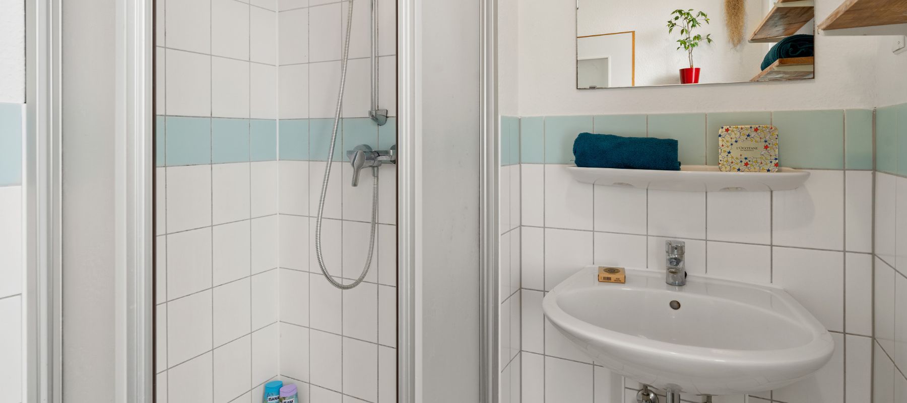 Gemeinschaftsbad in einer WG. Zu sehen ist ein Waschbecken mit Ablage und Spiegel darüber sowie eine Duschkabine.