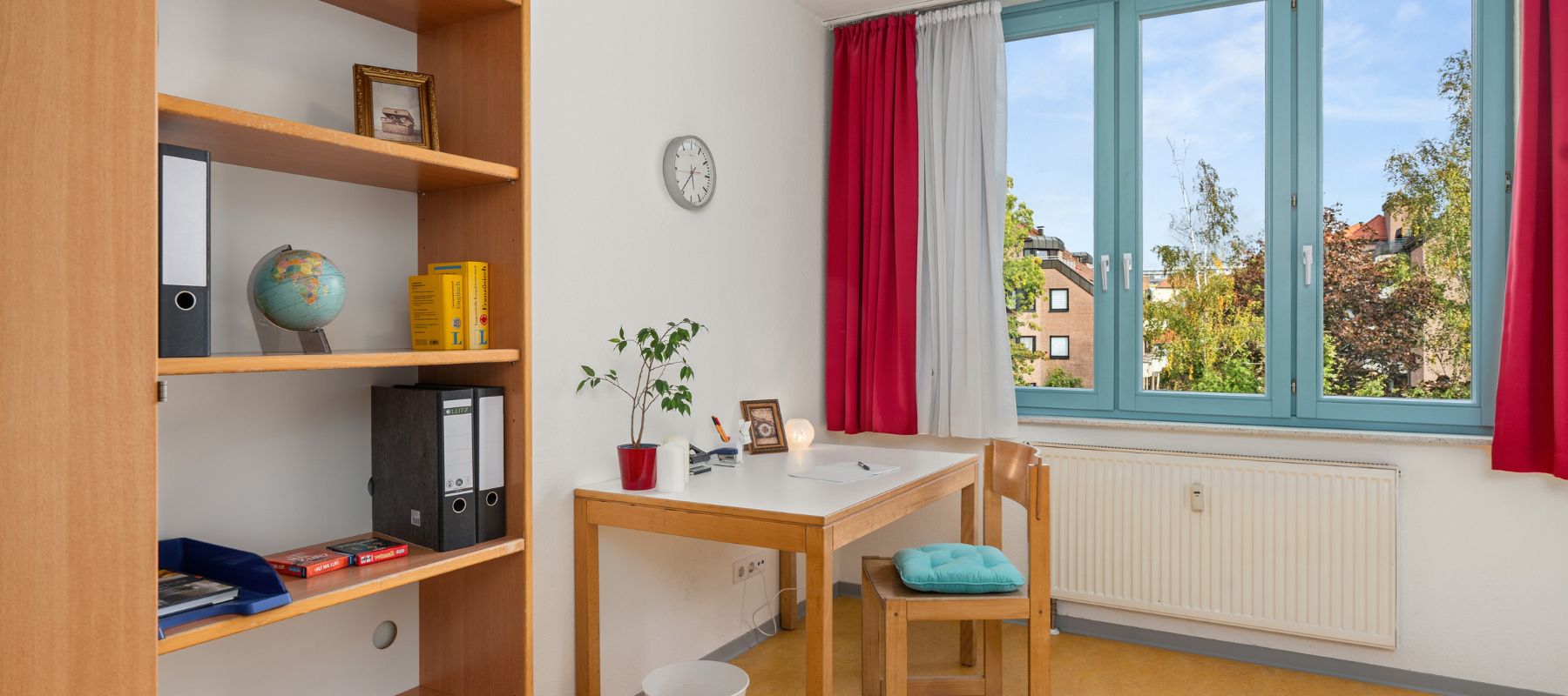 Blick in ein Einzelapartment: Zu sehen ist ein Schreibtisch mit Stuhl und ein Bücherregal.