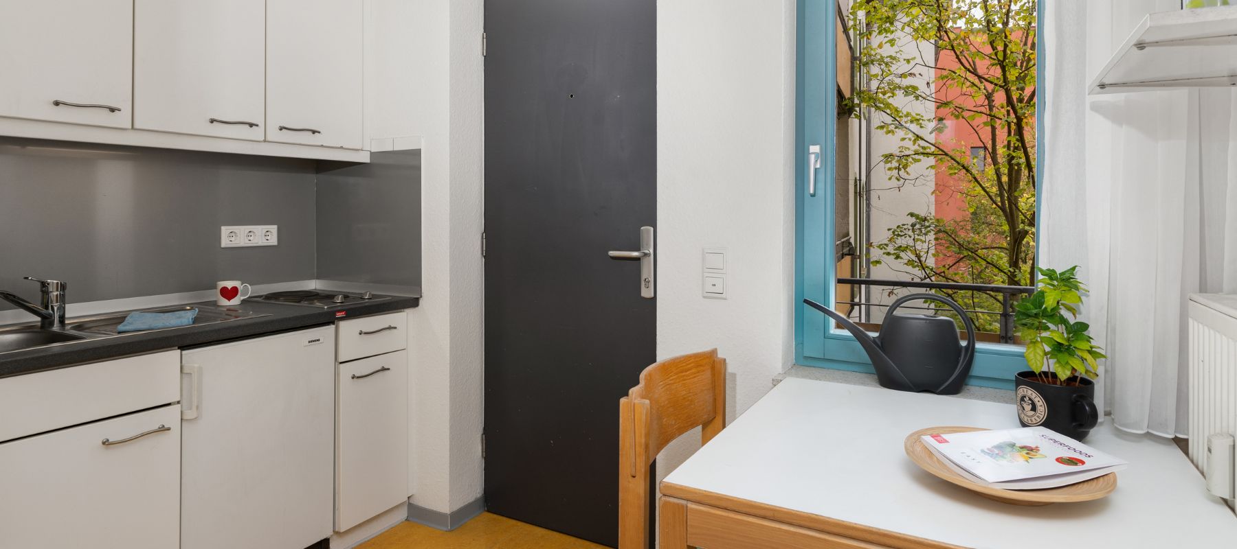 Küche eines Einzelapartments. Zu sehen ist ein kleiner Tisch mit Stuhl und eine Küchenzeile.