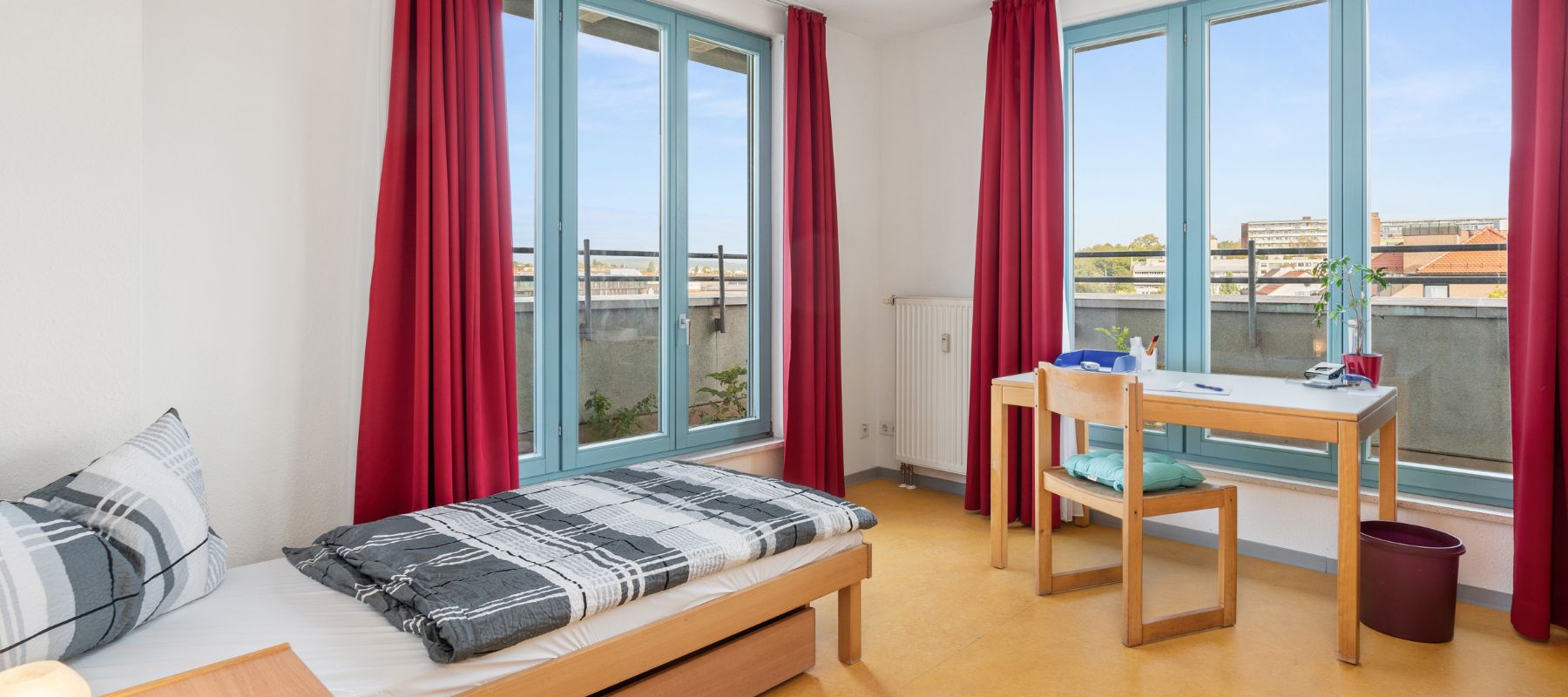 Einzelzimmer einer WG. Zu sehen sind Schreibtisch mit Stuhl sowie ein Bett.