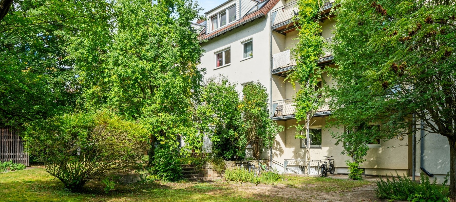 Der Garten auf der Rückseite der Naumburger Straße. Zu sehen ist viel Grünmit Bäumen, Büschen und einer Sitzbank.