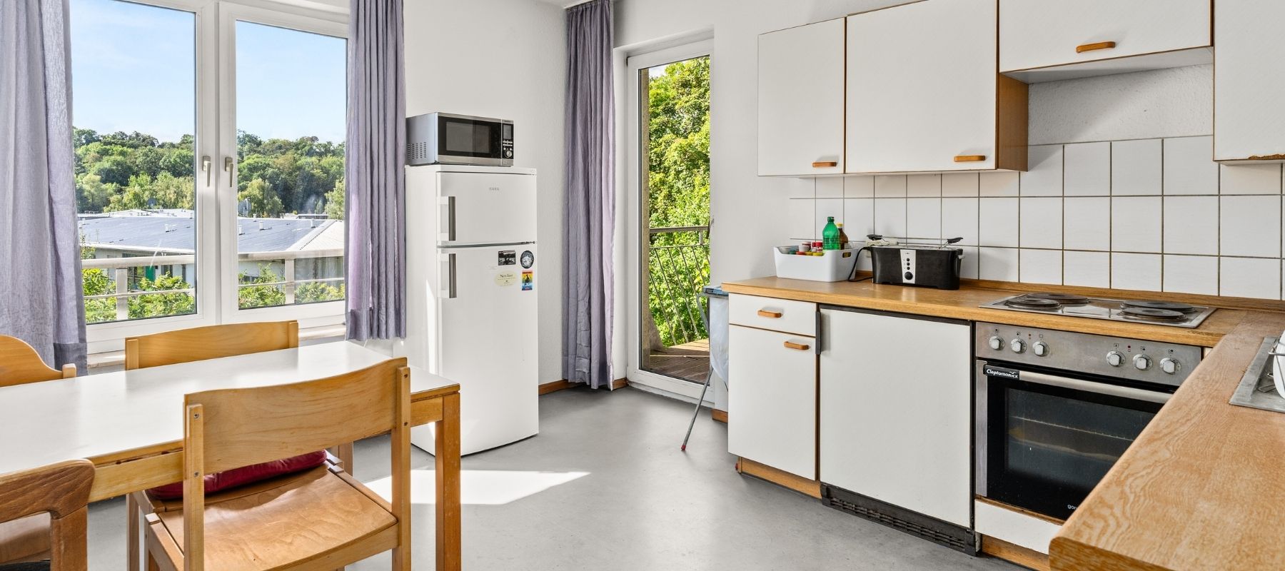 WG-Küche in der Naumburger Straße 13. Zu sehen ist ein heller Raum mit vielen Fenstern, einem Küchentisch mit Stühlen, einem Kühlschrank und einer Küchenzeile.