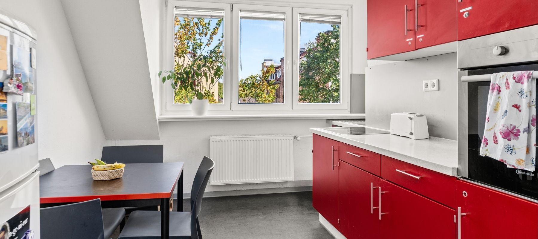 WG-Küche in der Naumburger Straße 15. Zu sehen ist eine Küchenzeile in Rot und Weiß, ein Küchentisch mit Stühlen und ein Kühlschrank.