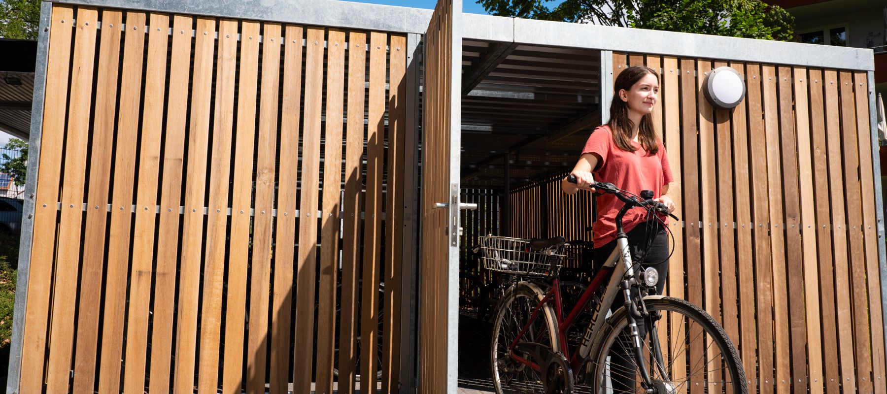 Fahrradschuppen. Zu sehen ist, wie eine Bewohnerin it ihrem Fahrrad aus dem Schuppen kommt.