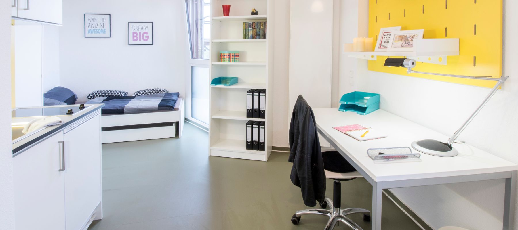 Einzelapartment im Wohnheim. Zu sehen sind Schreibtisch mit Stuhl, eine Küchenzeile sowie im Hintergrund ein Bett.