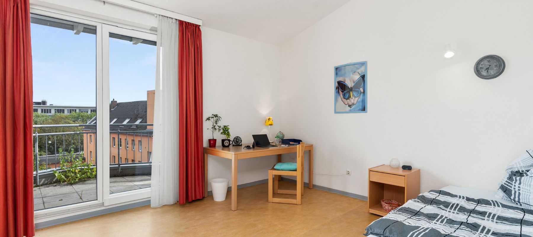 Einzelzimmer in WG mit Balkon. Zu sehen sind außerdem ein Schreibtisch mit Stuhl, ein Bett sowie ein Beistelltisch.
