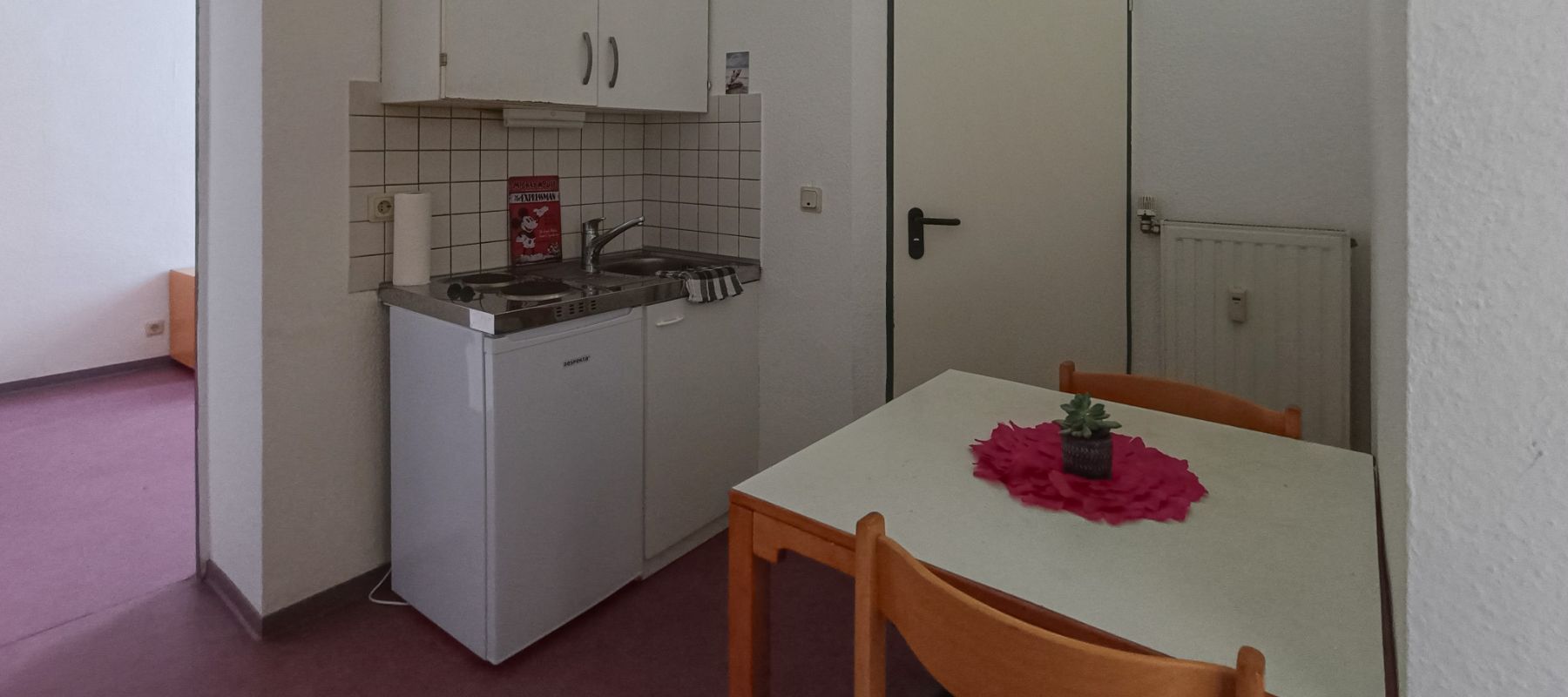 Küche eines Doppelapartments mit kleiner Spüle, einem Tisch und Stühlen.